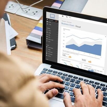 Visão sobre o ombro de um profissional digitando em um notebook que exibe um painel de análise de dados intitulado 'Business Chart - Visual', representando o fluxo de informações claras e o monitoramento estratégico na comunicação sistêmica organizacional.