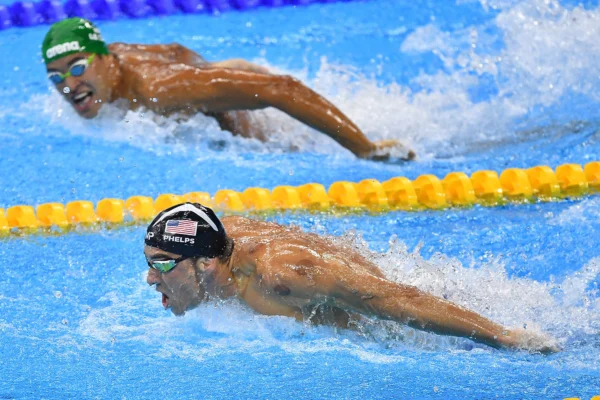 Fotografia de dois nadadores profissionais competindo em uma piscina durante a prova de nado borboleta, com o atleta em primeiro plano demonstrando foco extremo, ilustrando o conceito de desenvolver confiança, disciplina e alta performance.